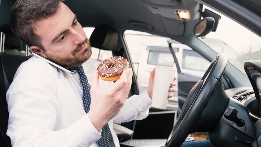 businessman-eating-donut-and-drinking-while-using-phone-in-his-car-1024x576.jpg